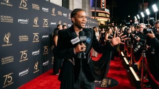 Celebrity stylist Law Roach speaking into press microphones on the Emmy Awards red carpet